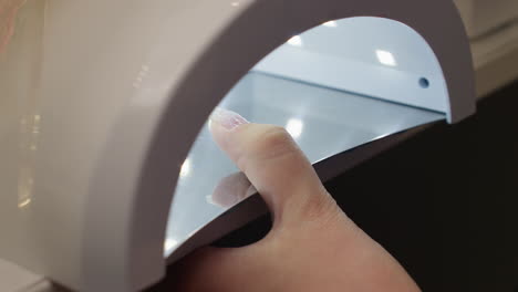 close-up view of customer placing thumb under led nail dryer to cure fresh polish. bright light activates while thumb is inside and shuts off immediately when finger is withdrawn from device