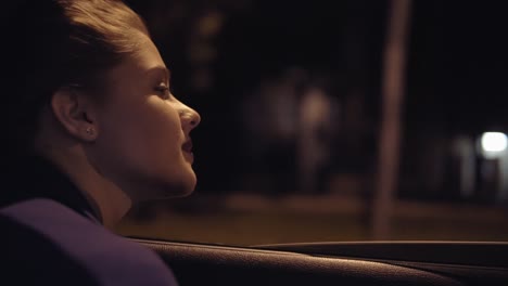 vista desde el coche: hermosa mujer joven inclinada desde la ventana del coche y mirando a la ciudad por la noche. disparo en cámara lenta