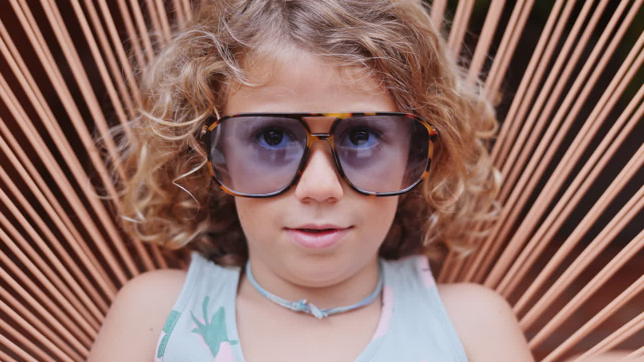 Cool little girl in a garden chair with sunglasses making faces