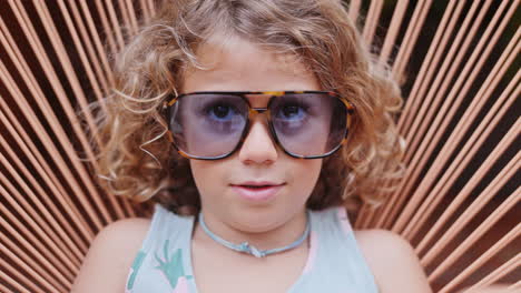 cool little girl in a garden chair with sunglasses making faces