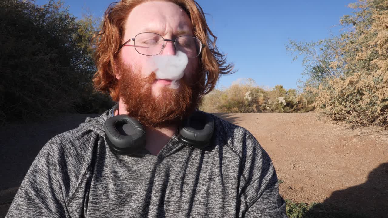 hombre pelirrojo vaping en el desierto.