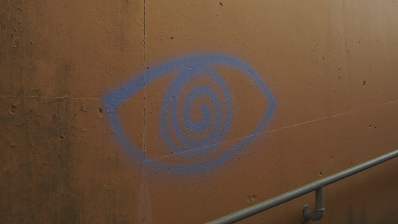 Blue spiral eye graffiti on a weathered concrete wall near a metal railing