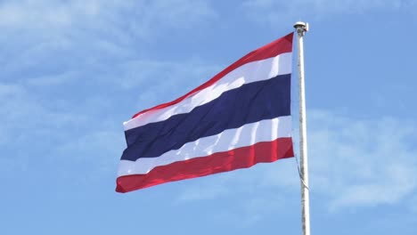 waving the kingdom of thailand flag on a pole with blue sky and white clouds in the background