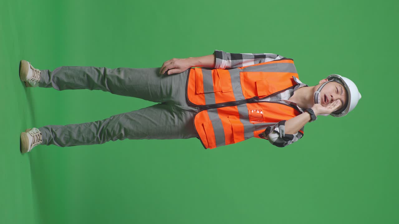 Full Body Of Asian Male Engineer With Safety Helmet Yelling With Hand Over Mouth While Standing In The Green Screen Background Studio