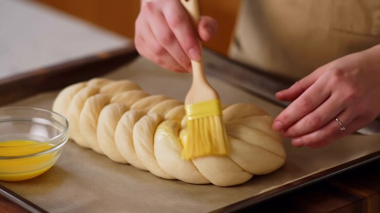 Baker Brushing Egg Wash On Braided Loaf, Pastry Chef Hands Gently Coat Braided Dough With Glossy Egg Wash