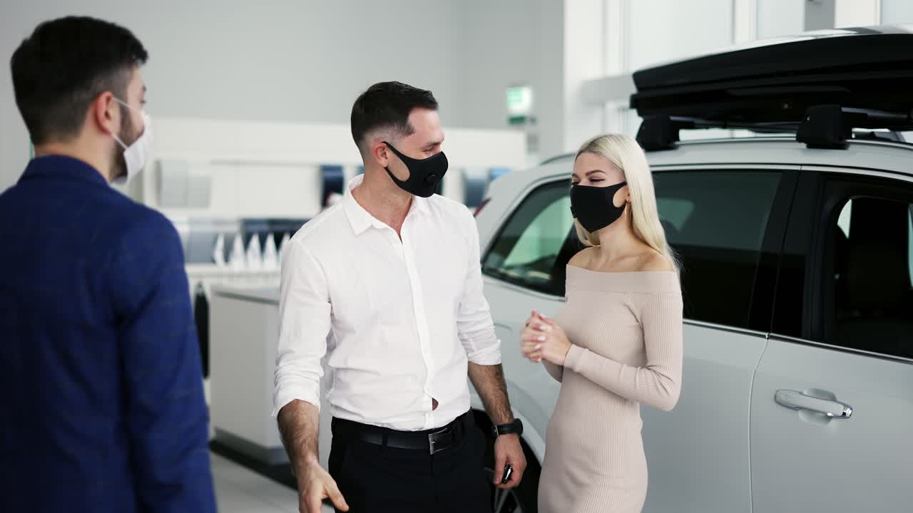 nuevos propietarios de automóviles recibiendo las llaves de automóviles de lujo comprados en el concesionario, usando máscaras