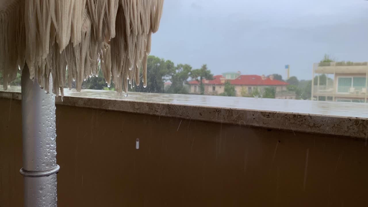 las gotas de lluvia caen sobre el parapeto y la sombrilla doblada en el balcón