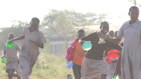 school children eagerly run for lunch as bell rings, playful scene in african schoolyard holding porridge bowls, slow motion