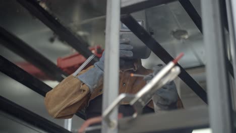 welder takes off protective mask to check his work on metal frame