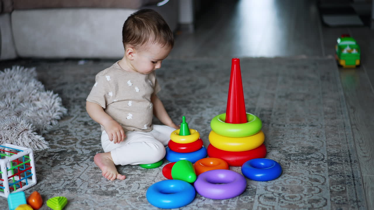 Smart little boy plays with his toys on the floor. Lovely baby assembling the pyramids. High angle view.