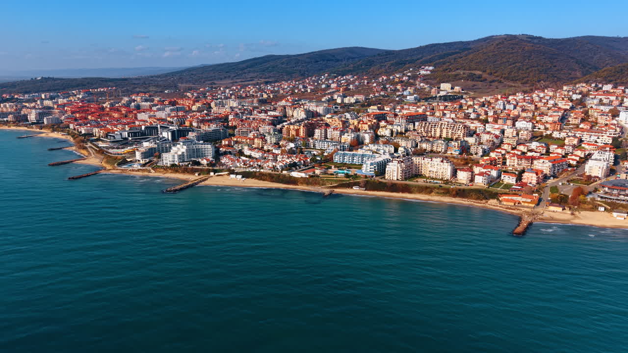 Resort binalarıyla dolu sahil şeridinin geniş açılı havadan çekilmiş görüntüsü. Oteller, plajlar ve arka planda yemyeşil tepeler içeren deniz kıyısının panoramik manzarası