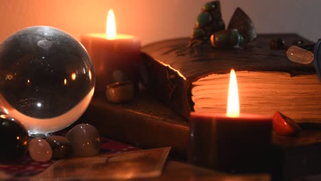 Background of a fortune teller table covered with fabric, with crystal balls, stones, cards, ancient books, rings and candles with flickering flames