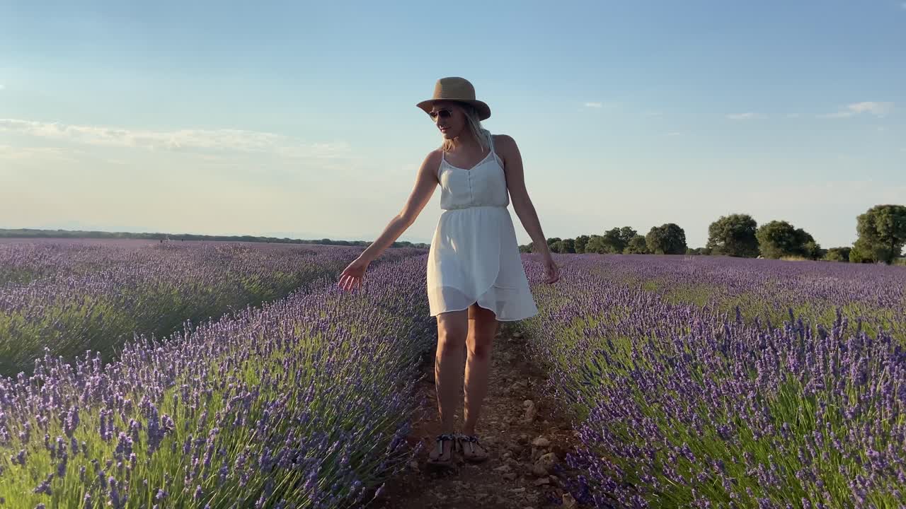 Woman in a white dress walks to the camera in a rural lavender field