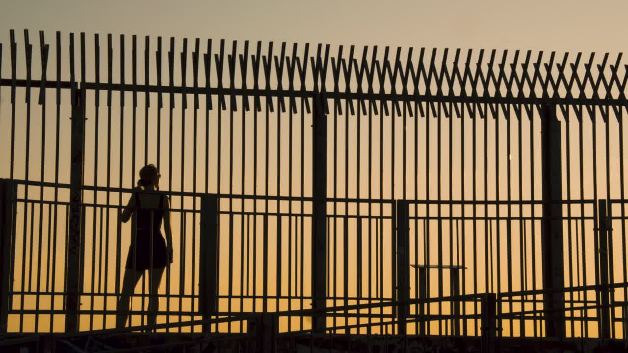 일몰 동안 울타리 앞에서 걷는 젊은 여성의 실루엣