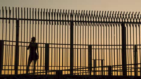 silueta de mujer joven caminando frente a la cerca durante la puesta de sol