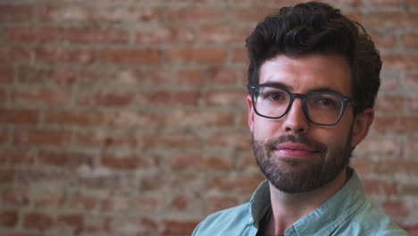 hombre caucásico sonriente con barba y gafas de pie contra la pared de ladrillo en la cafetería