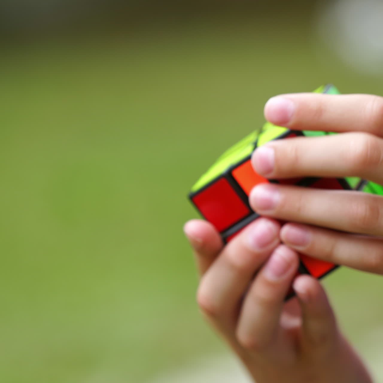 Young person solving a Rubik's cube puzzle. Smart boy tries to finish solving colorful combination in Rubik's Cube on green background. Close-up.