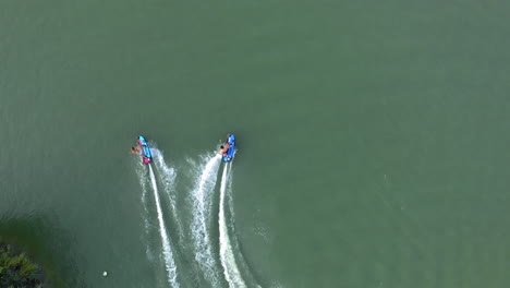 Two-people-on-jetsurf-boards-racing-each-other-around-a-watersport-recreational-area,-aerial-god-view,-slow-motion