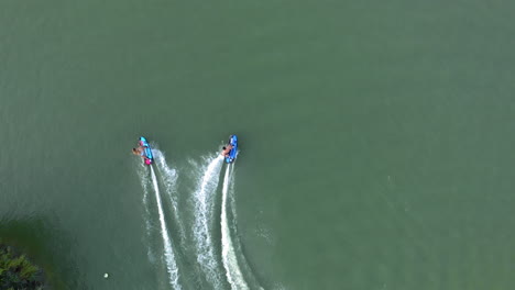 two people on jetsurf boards racing each other around a watersport recreational area, aerial god view, slow motion