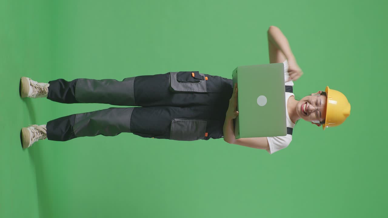 cuerpo lleno de mujer asiática trabajadora con gafas de protección y casco de seguridad mirando la computadora portátil luego gritando gol celebrando mientras estaba de pie en la pantalla verde estudio de fondo