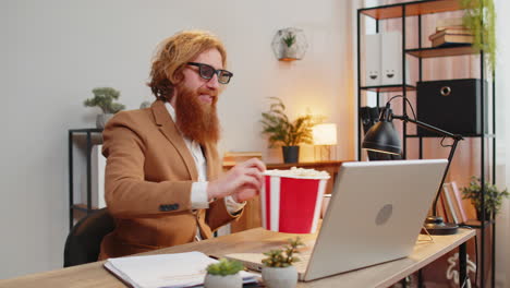 Business-man-taking-break-from-work-wearing-3D-glasses-earing-popcorn-watching-movie-on-laptop