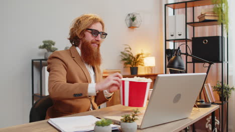 business man taking break from work wearing 3d glasses earing popcorn watching movie on laptop