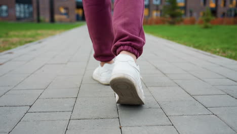 back leg view of hoodie wearing athlete striding on grey tiled pavement in urban park setting beside blooming spring foliage with playground bars in background conveying active lifestyle
