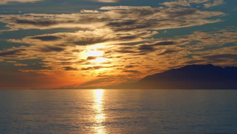 puesta de sol nublada en el mar con silueta de montañas en el fondo