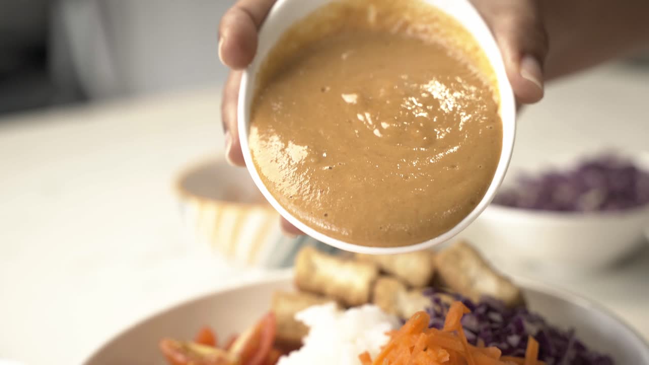 Close up of Homemade tahini sauce pouring on rice for poke bowl recipe dish
