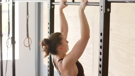 mujer caucásica sin alteración enfocada entrenando en el gimnasio haciendo abdominales en barras, en cámara lenta