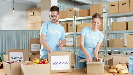 caucasian young male and female volunteers packing box with food in charity warehouse