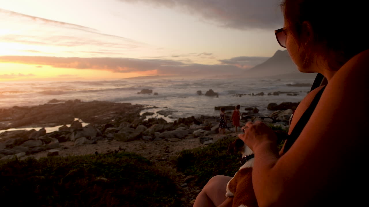Madre con perro mascota observando a niños jugar en la costa al atardecer