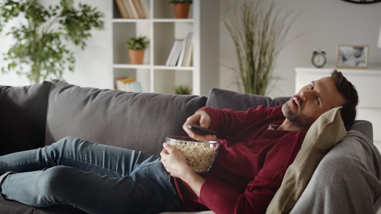 video de un hombre aburrido viendo televisión en casa