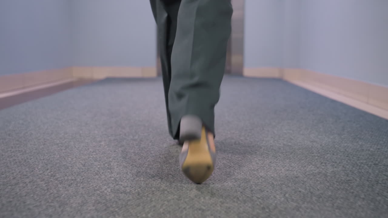 Back view of businesswoman walking confidently in office, wearing stylish gray shoes on office carpet floor, showcasing professional attitude and fashion