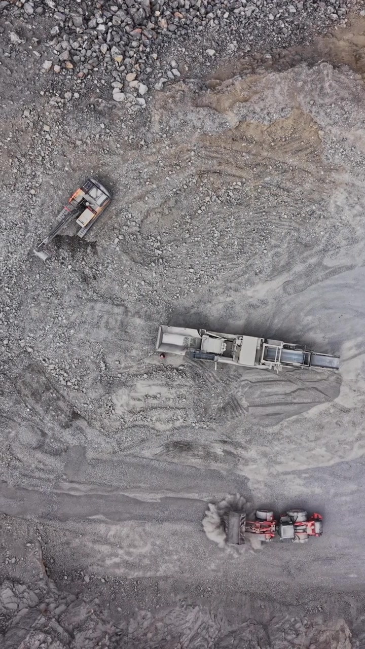Construction vehicles operate in a gravel pit during daytime work hours