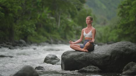 attractive european blond female sitting on rock in lotus position, nature healing