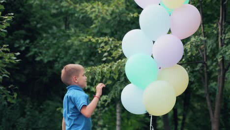 a cheerful and happy boy is playing and jumping in the park for birthdays near a big bunch of colorful balloons