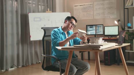Asian Man Engineer With A Laptop Thinking While Holding Paper Model Of House At The Office