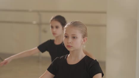 a group of young ballet students in black dancewear practicing positions in a spacious ballet studio with wooden flooring and wall-mounted barres. focused expressions and synchronized movements.