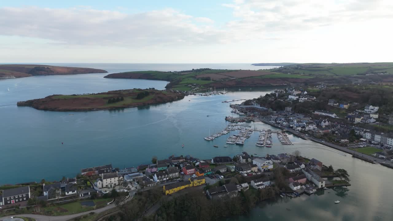 Backwards flying drone over Kinsale town and river reflecting clouds in Ireland, calm evening.