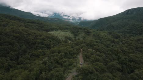 Aerial-view-of-a-white-Cherokee-truck-driving-trhough-the-forest-in-a-spectacular-moutain-landscape,-drone-shot