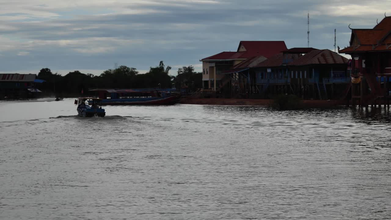 A wide shot of a floating village community along the river in Cambodia, with stilt houses and boats surrounded by lush flooded forest.
