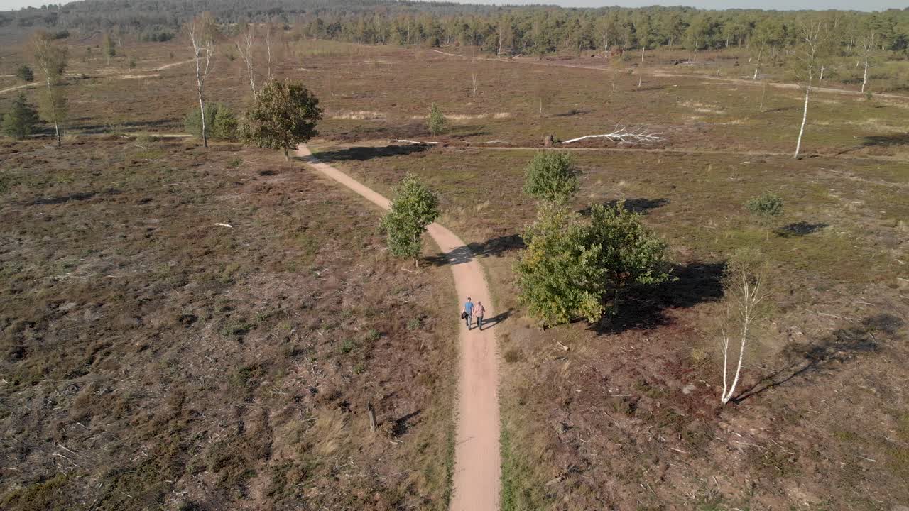 vista aérea de una pareja de ancianos caminando por un sendero a través de un paisaje de páramos