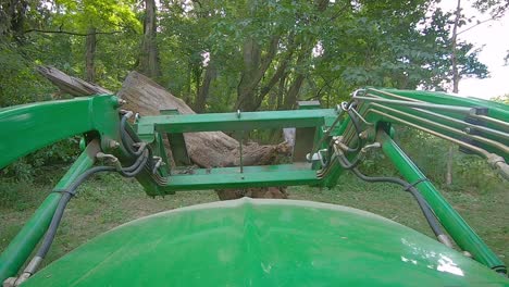 pov of equipment operator moving large stump with roots in a yard using a loader with forks in an yard surrounded by woods