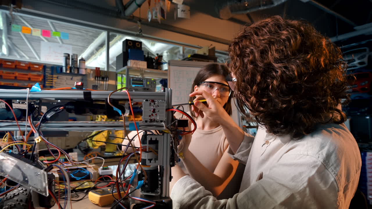 Young man and woman in protective glasses doing experiments in robotics in a laboratory. Robot and tools on the table