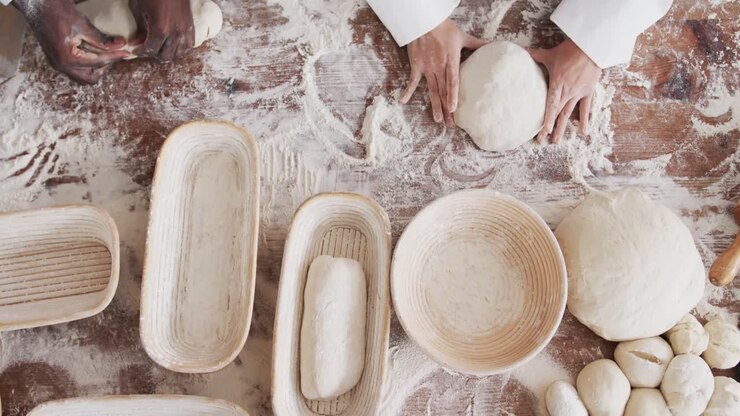 Midsection of diverse bakers working in bakery kitchen, forming bread form dough, slow motion
