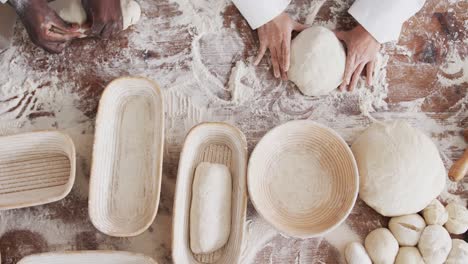 midsection of diverse bakers working in bakery kitchen, forming bread form dough, slow motion