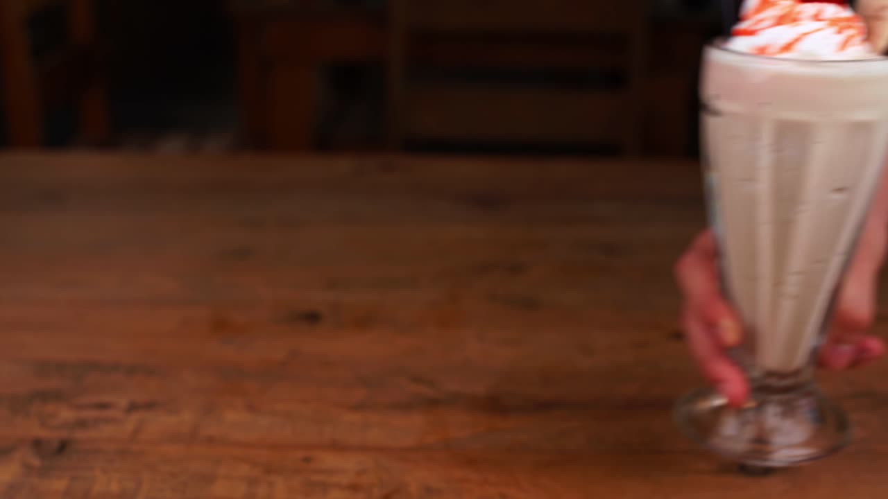 un primer plano detallado de un batido de chocolate, con caramelo, espresso y crema batida y caramello, siendo entregado a la mesa.