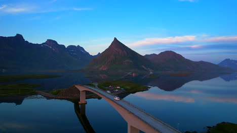 Luftaufnahme-Eines-Umgebauten-Lieferwagens,-Der-über-Die-Berühmten-Brücken-Fredvang-Auf-Den-Lofoten-Inseln-Fährt,-Wobei-Sich-Volandstind-Auf-Dem-Wasser-Spiegelt