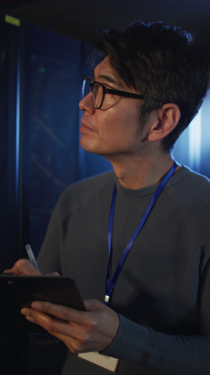 Vertikal video af asiatisk mand, der bruger tablet og arbejder i et serverrum